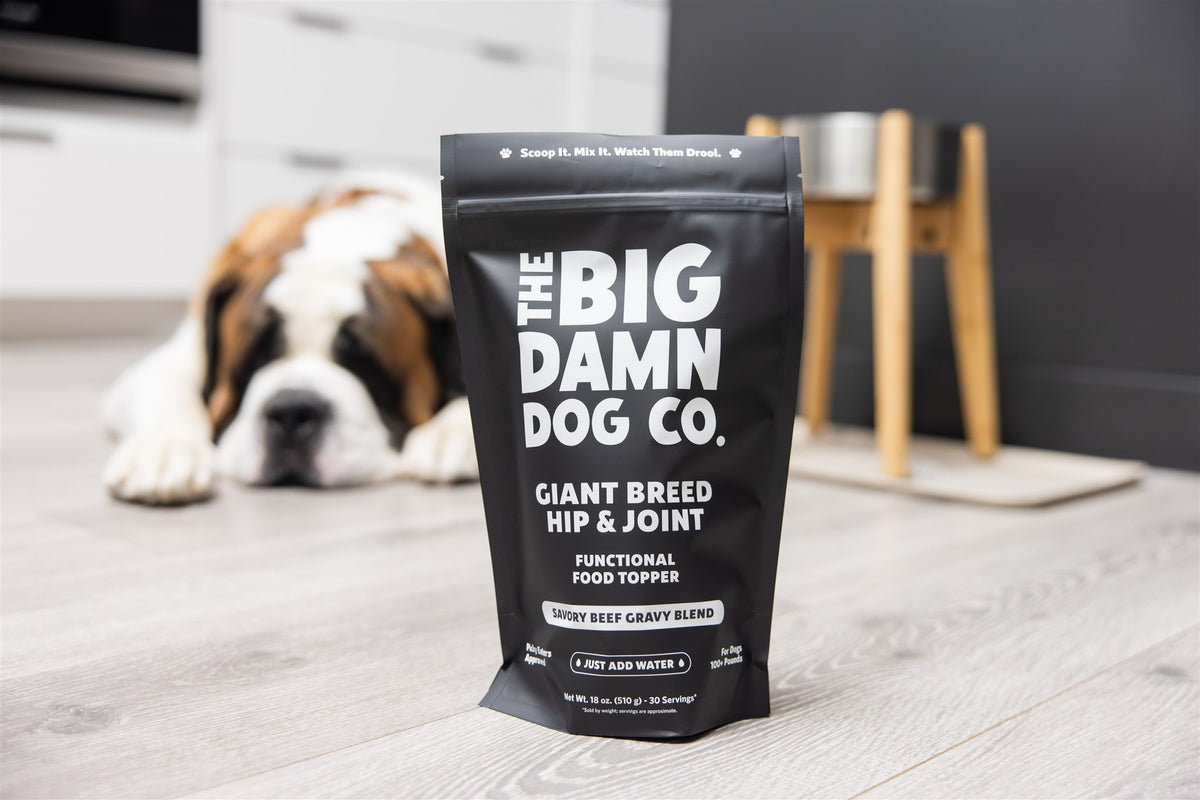 Dog food package from The Big Damn Dog Co. on a wooden floor with a dog in the background.