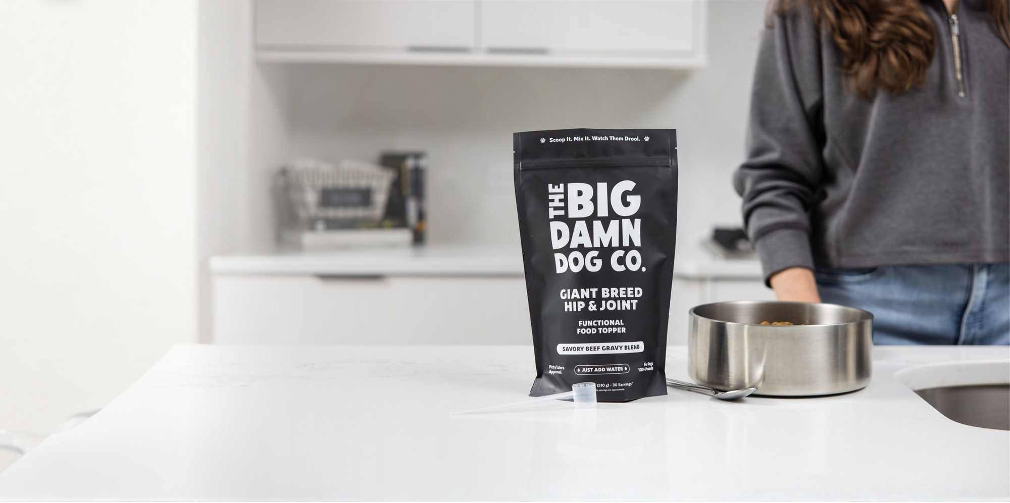Bag of Big Damn Dog Co. dog food on a kitchen counter with a person in the background.